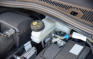 Close-up of a car engine bay showcasing a brake fluid reservoir with a black cap labeled DOT 4, surrounded by wiring and other engine components, highlighting the importance of regular brake service.