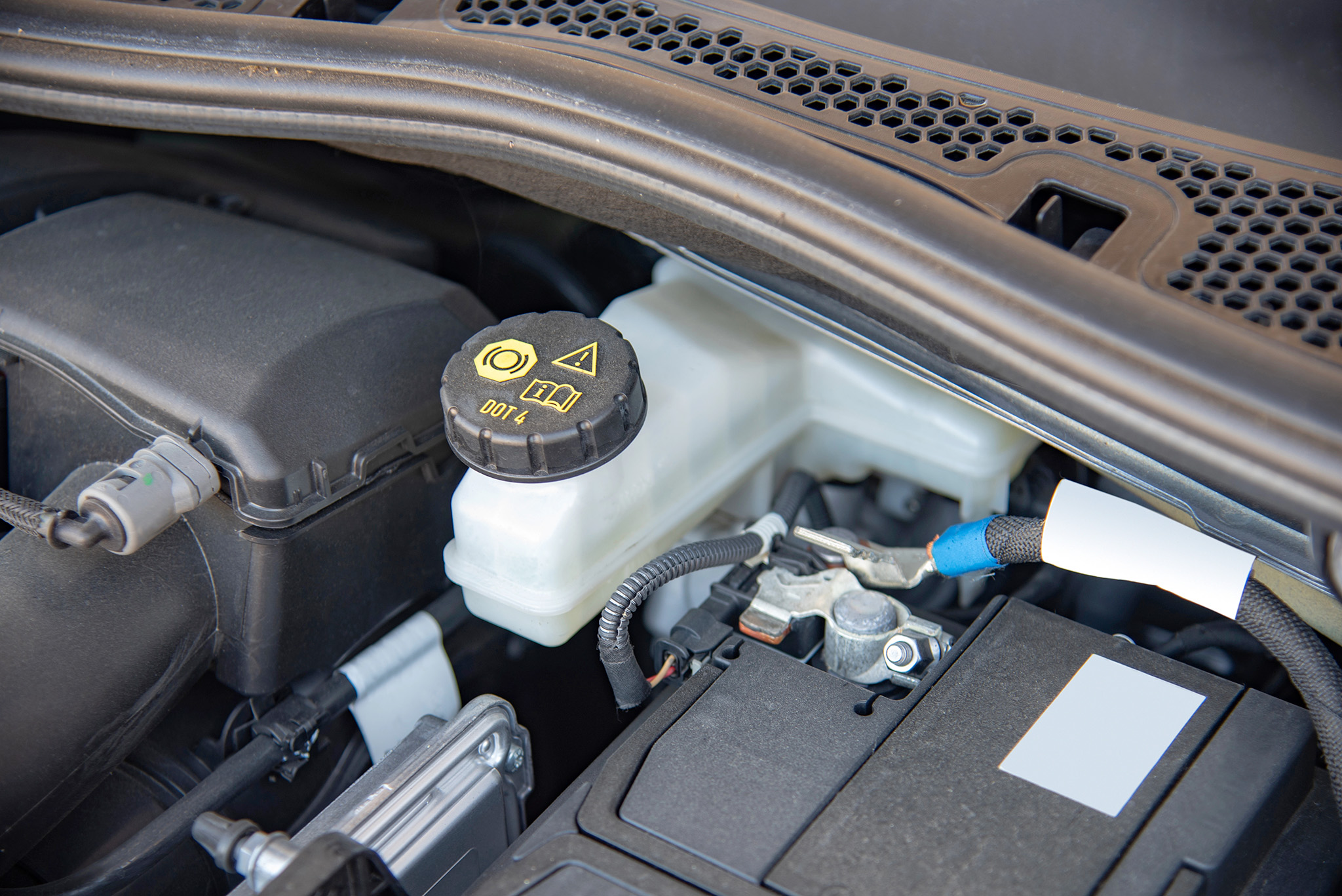 Close-up of a car engine bay showcasing a brake fluid reservoir with a black cap labeled DOT 4, surrounded by wiring and other engine components, highlighting the importance of regular brake service.