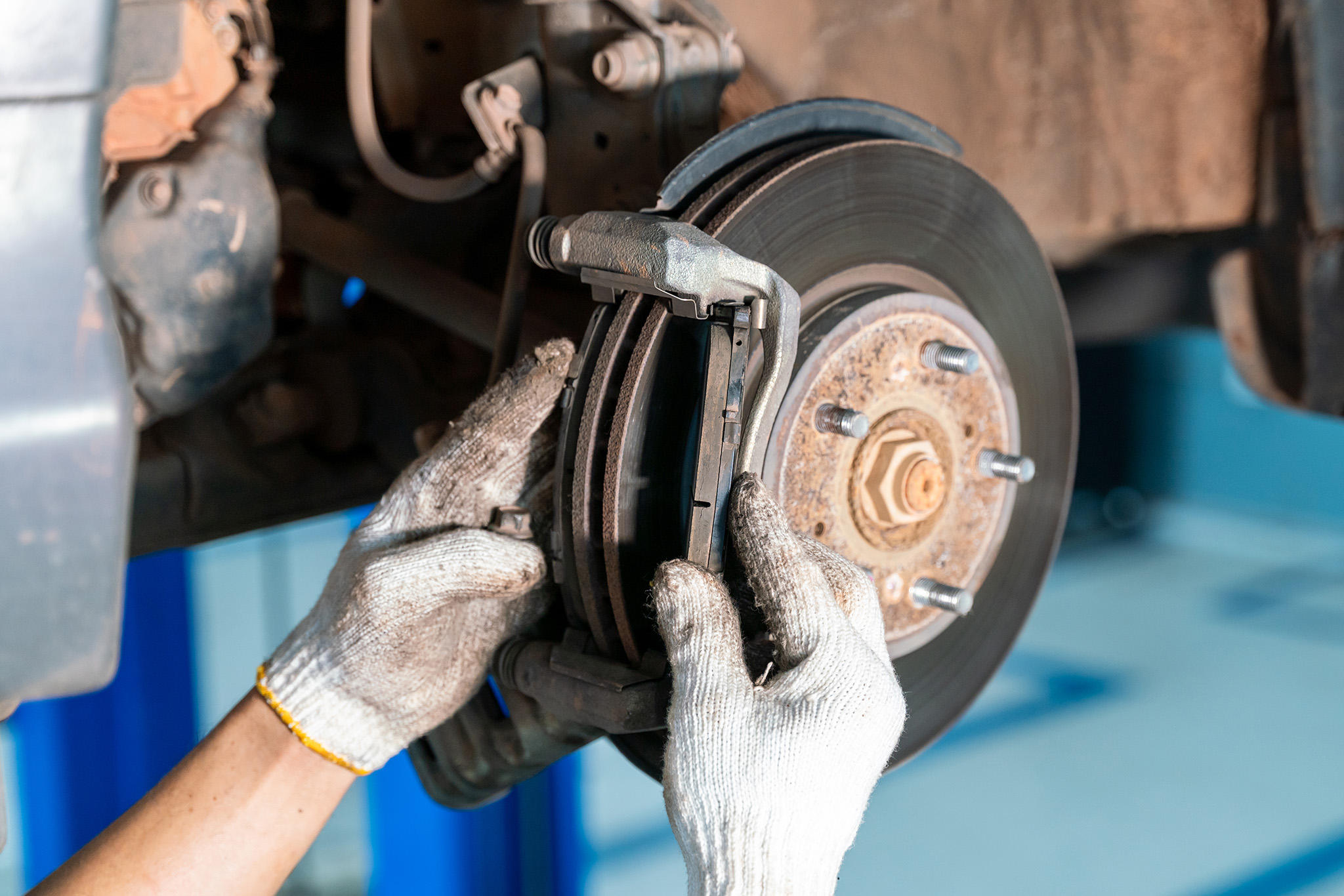 A mechanic with white gloves expertly provides brake service, meticulously working on a vehicle's brake disc and caliper in the garage.