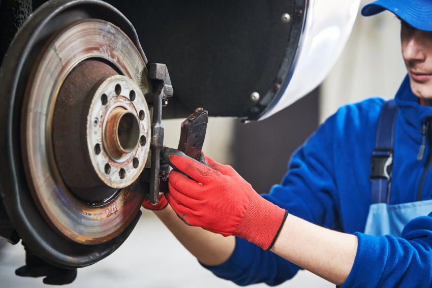 A mechanic wearing red gloves inspects a car's brake disc and pad.