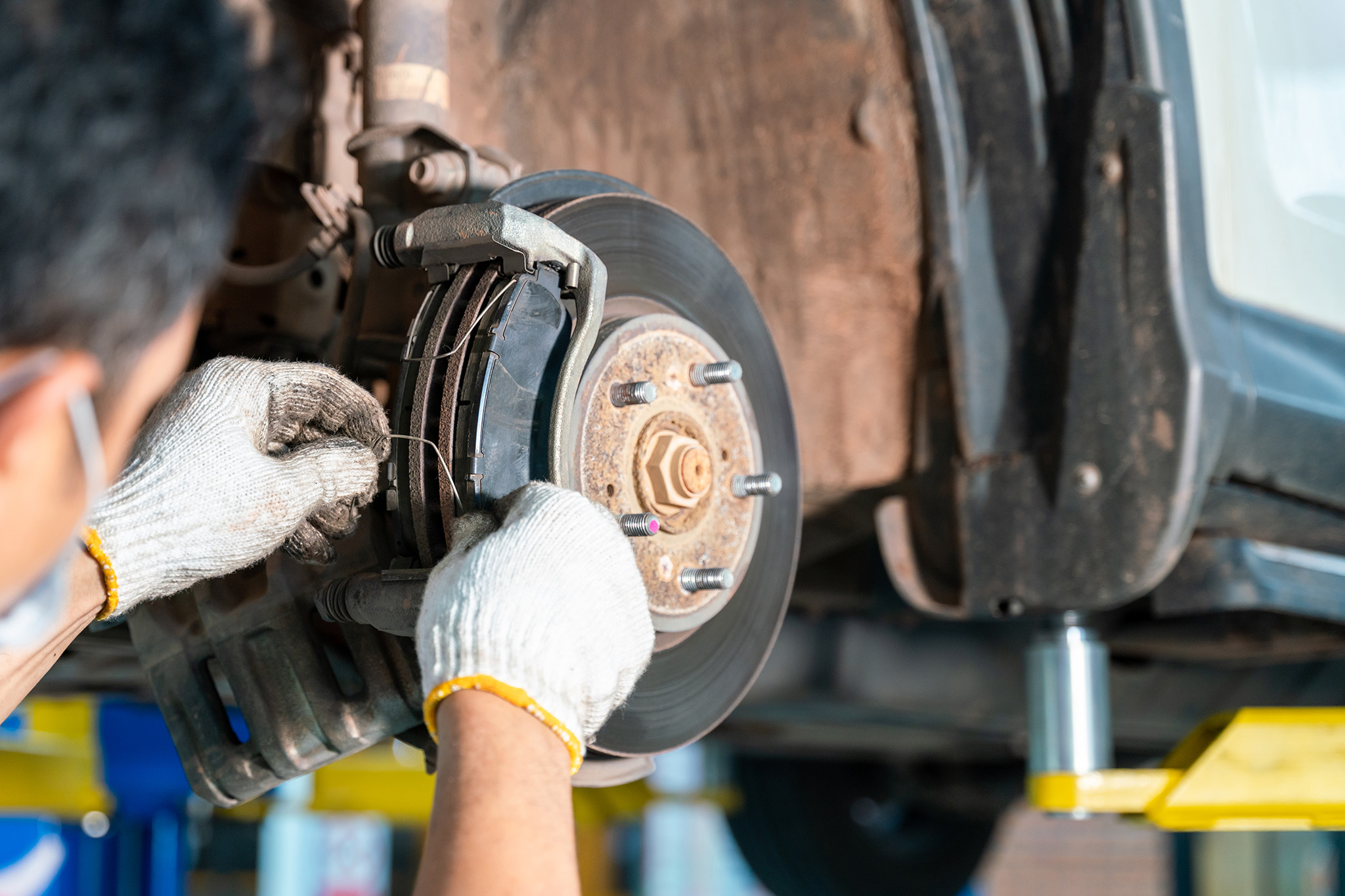 The mechanic, wearing gloves, inspects the car's brake system on a lift, ensuring top-notch brake service for optimal safety.