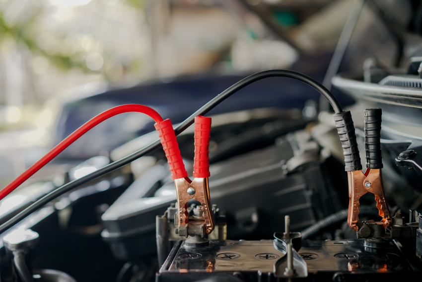 Close-up of jumper cables, with red and black clamps connected to a car battery in an engine bay.