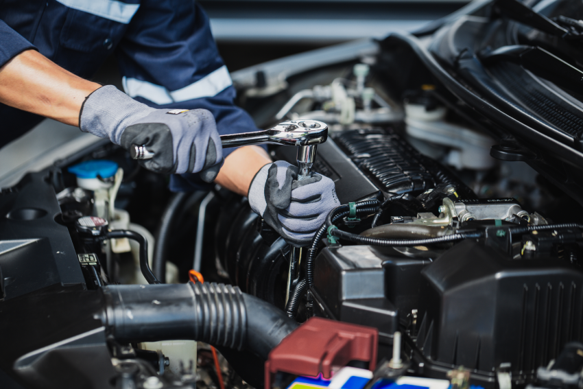 Mechanic using a ratchet wrench on a car engine wearing gloves and a uniform.