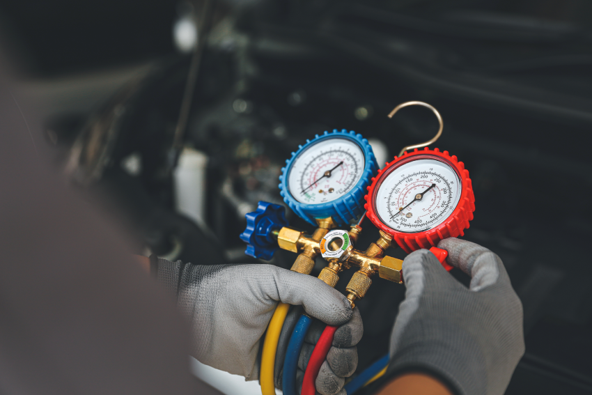 A person in gloves adjusts a manifold gauge set with red and blue dials, used for air conditioning system diagnostics.