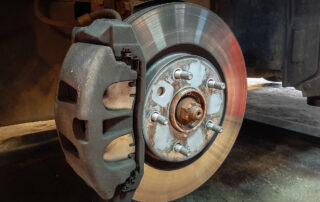 Close-up of a car's exposed disc brake and caliper, with six lug nuts visible, set against a vehicle's wheel hub in a garage environment, highlighting the importance of regular brake service.