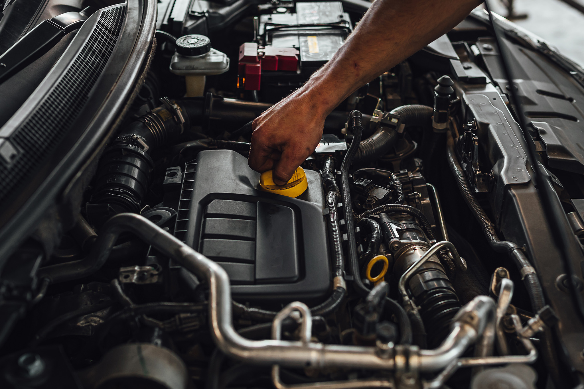 Person's hand unscrewing the oil cap in a car engine bay, preparing for an oil change in Monument CO.