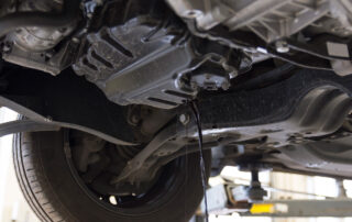 Underneath a vehicle on a lift, oil is dripping from the oil pan near the wheel assembly in the car’s chassis. If you need an expert inspection or an Oil Change Monument CO can trust, visit our skilled technicians to keep your car running smoothly.