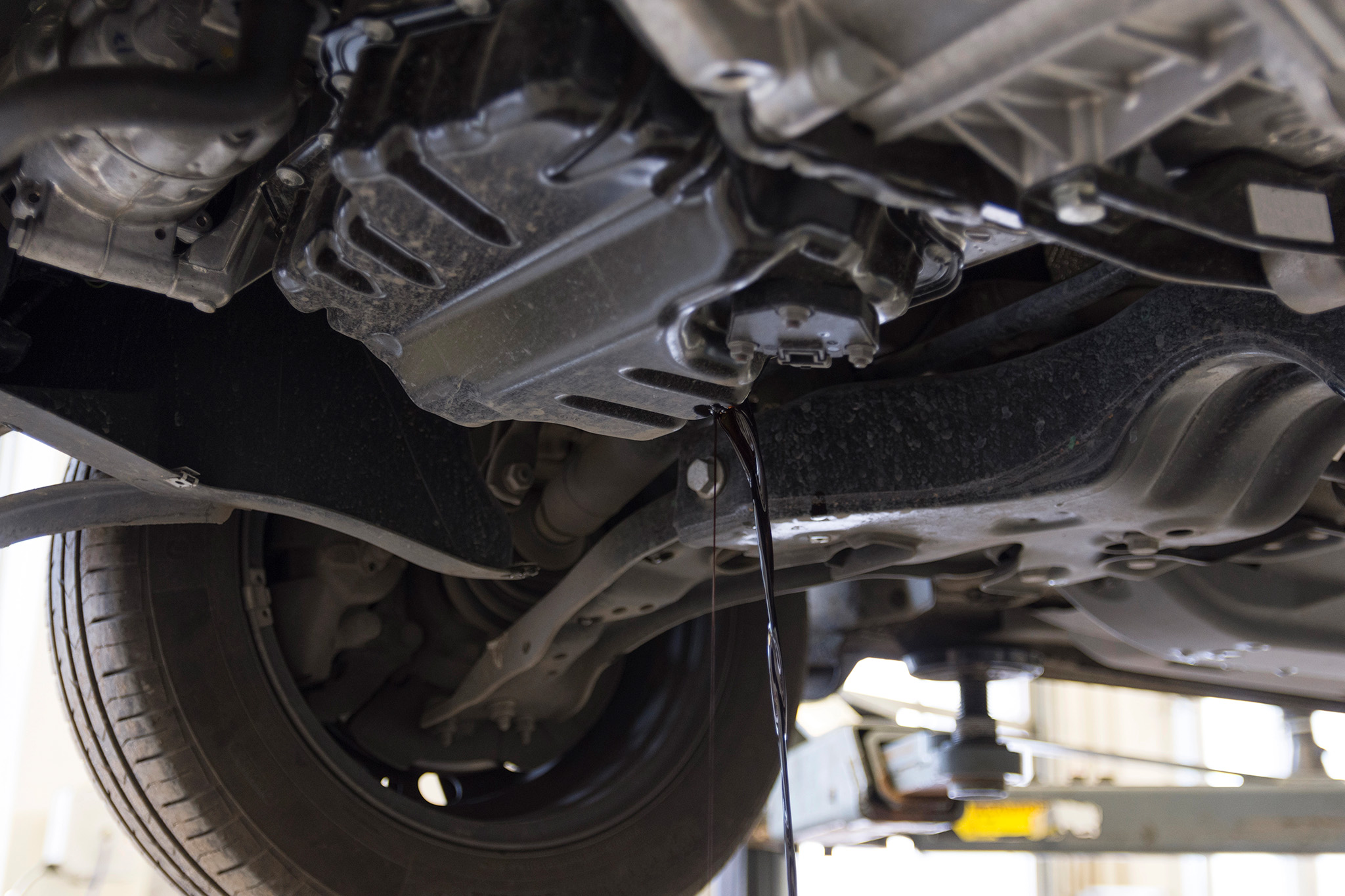 Underneath a vehicle on a lift, oil is dripping from the oil pan near the wheel assembly in the car’s chassis. If you need an expert inspection or an Oil Change Monument CO can trust, visit our skilled technicians to keep your car running smoothly.