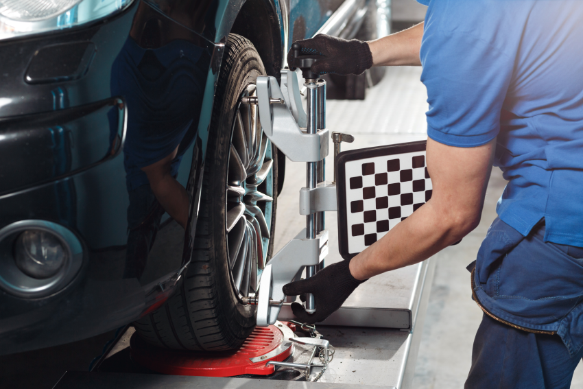 Mechanic wearing gloves performs a wheel alignment on a vehicle using specialized equipment at a garage.