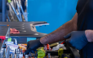 A person wearing gloves is organizing tools and equipment in a workshop. Various wrenches, screwdrivers, and power tools are visible.