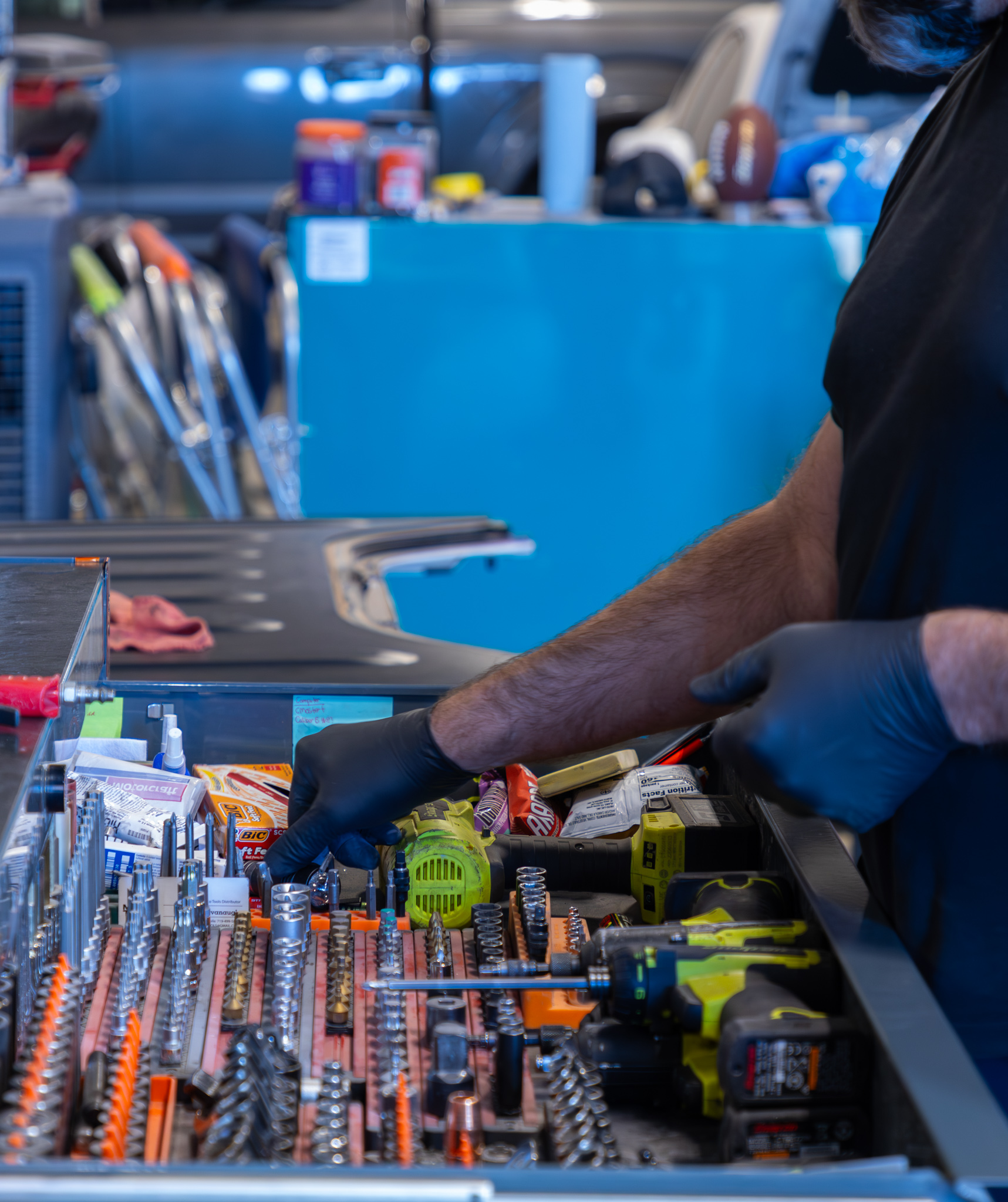 A person wearing gloves is organizing tools and equipment in a workshop. Various wrenches, screwdrivers, and power tools are visible.