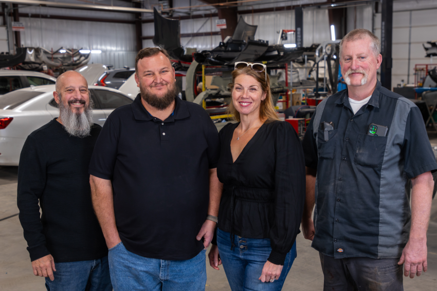 Bill & Stephanie Ellison, Matt & Paul, standing in a garage with vehicles and tools in the background.