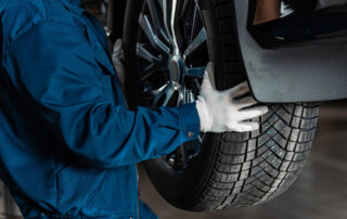 In an auto service shop, a mechanic in blue coveralls and white gloves meticulously inspects a car tire on a vehicle lift.
