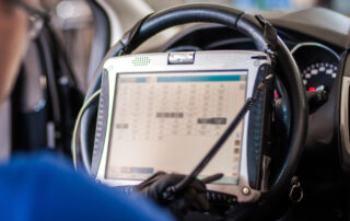 In the bustling auto service shop, a technician expertly uses a diagnostic tablet mounted to the steering wheel, analyzing real-time data inside the vehicle with precision.