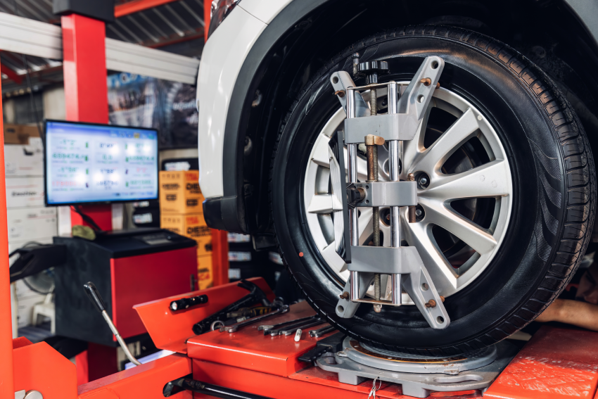 A car tire on a wheel alignment machine, with a monitor displaying alignment data in the background.