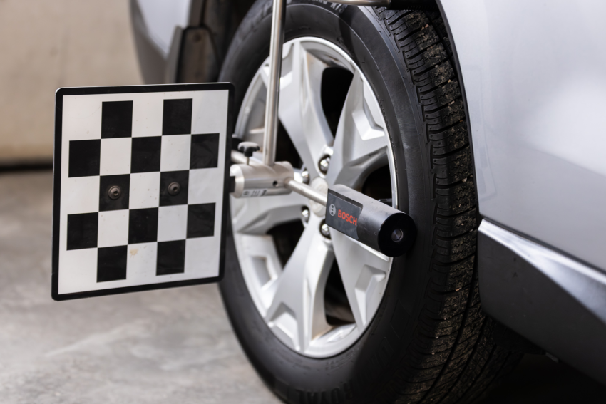 Car wheel alignment tool attached to a vehicle's front tire, with a checked calibration target plate and alignment equipment visible.