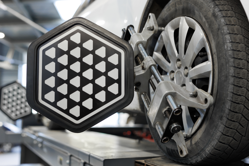 A car wheel on an alignment machine with a geometric-patterned sensor attached, inside an automotive repair shop.