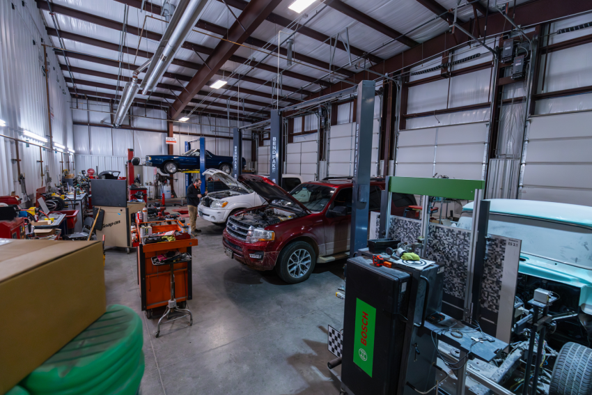 Auto repair shop interior with vehicles parked, including a red SUV with its hood open, and various tools and equipment scattered around.