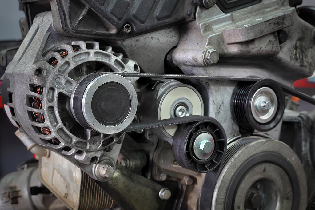 Close-up of a car engine with visible belts and pulleys, showcasing various components like the alternator, tensioner, and fluid flush system in a mechanical setup.