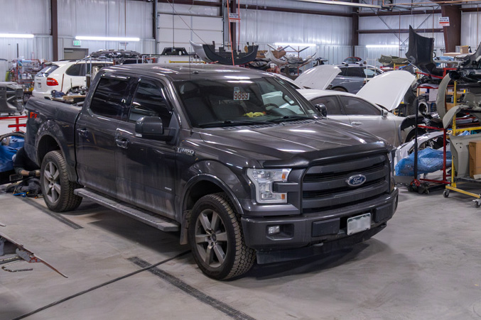 A black Ford F-150 truck sits in a bustling tire shop, surrounded by other vehicles and repair equipment.