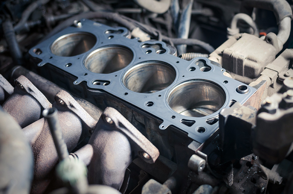 Close-up of an engine block with four visible cylinder bore holes, showcasing parts of a gasket and intake manifold in a workshop setting. This detailed view highlights the precision involved in engine repair.