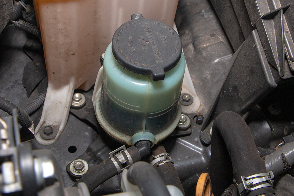 Close-up of a car engine's coolant reservoir and hoses, showing a black cap and greenish fluid inside, highlighting the importance of regular fluid flush maintenance for optimal performance.