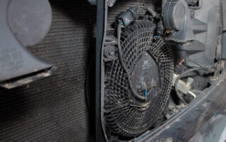 Close-up of a car radiator fan and shroud inside an engine compartment, ready for a fluid flush. The fan is encased in a circular, grid-patterned cover.